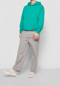 Tyrkysová mikina s kapsou na přední straně, spárovaná s lehkými šedými volnými kalhotami a vzorovými teniskami s multikulturními akcenty.