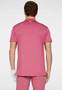 Kortärmad polo i ljusrosa, tillverkad av slät tyg med krage, med en liten logotyp på baksidan och avslappnad passform.