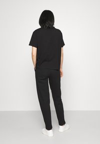 Camiseta de algodón negra y joggers a juego, corte relajado, textura suave, usados con zapatillas blancas, vistos desde la parte posterior sobre un fondo liso.