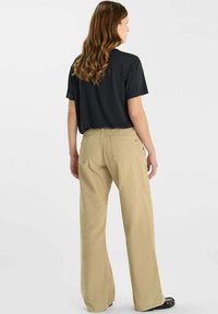 Zwarte kortarmig shirt gecombineerd met beige wijde broek. De broek heeft twee achterzakken en een gestructureerde afwerking. Beide kledingstukken zijn van achteren getoond.