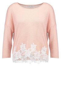 Maglione rosa chiaro con vestibilità ampia e maniche a tre quarti. Presenta un bordo in pizzo bianco nella parte inferiore, creando un contrasto testurizzato.