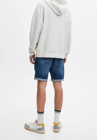 Felpa con cappuccio grigia chiara, pantaloni shorts in denim con risvolti, sneakers bianche con dettagli grigi e gialli, e calze a righe verdi.