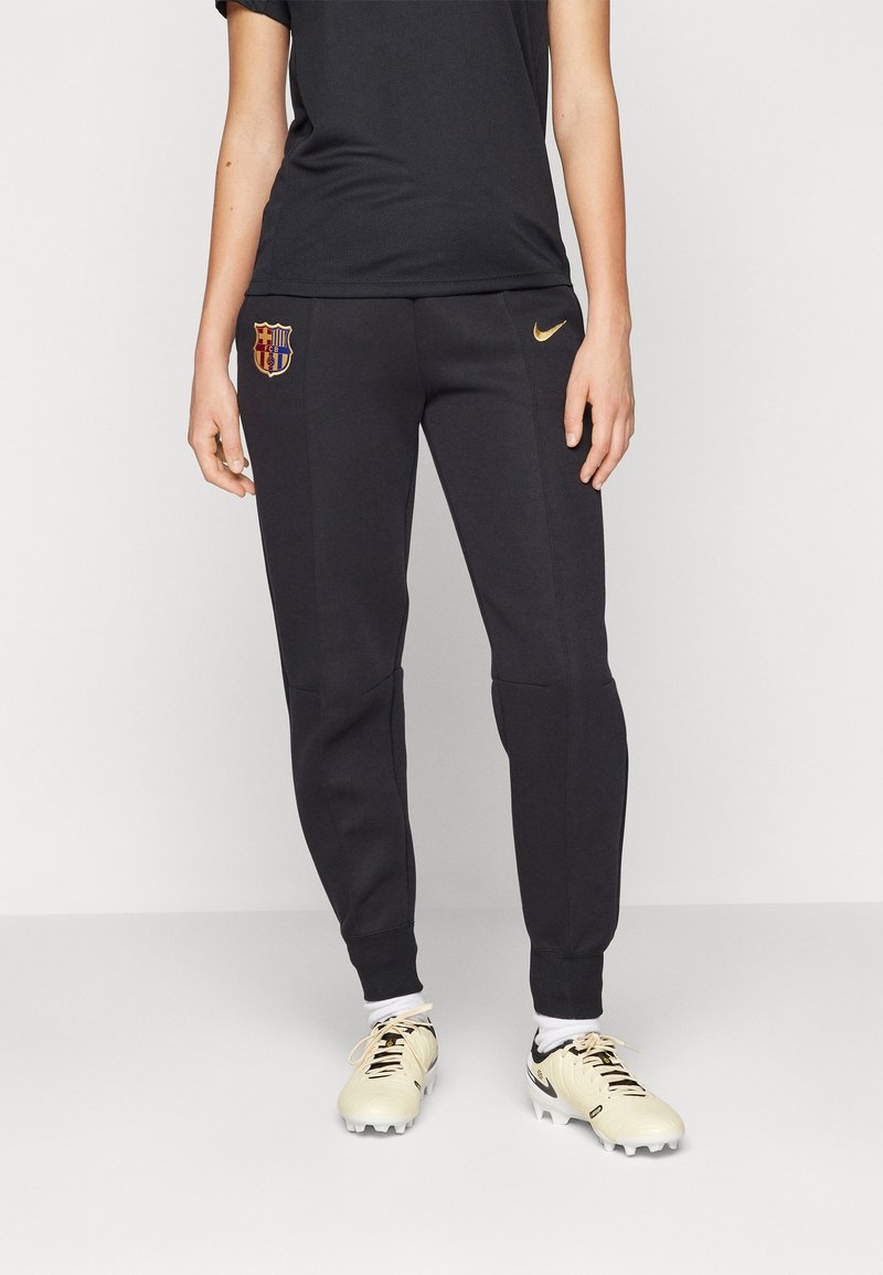 Pantaloni felpati neri con un design aderente, caratterizzati da un emblema del Barcellona e un logo Nike dorato sulla coscia. Il materiale è morbido con polsini elastici.