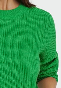 Zielony sweter dzianinowy z teksturowanym wzorem, z okrągłym dekoltem i lekko podwiniętymi rękawami dla swobodnego fasonu.