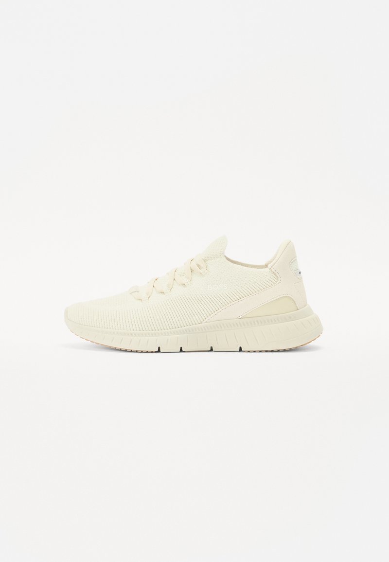 Lys beige sportsko med en teksturert strikket overdel, snøring og en ribbet gummisåle. Har en subtil logo på siden.