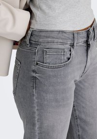 Jean denim gris avec une coupe ajustée, des coutures apparentes et des poches avant. Le tissu présente une texture lisse et un léger effet délavé.