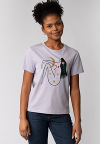 T-shirt en coton violet avec un design graphique d'une figure allongée entourée d'étoiles, de lune et d'éléments végétaux avec des accents verts, dorés et rouges.