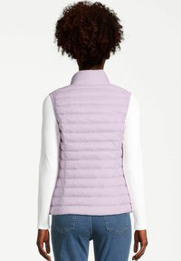 Chaleco acolchado morado sin mangas con diseño de acolchado horizontal. Textura suave, cuello alto, usado sobre una camisa blanca de manga larga y jeans azules.