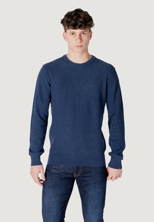 Maglione a maglia blu navy con scollatura rotonda, motivo a trama texturizzata, polsini e orlo a coste. Abbinato a jeans blu scuro.