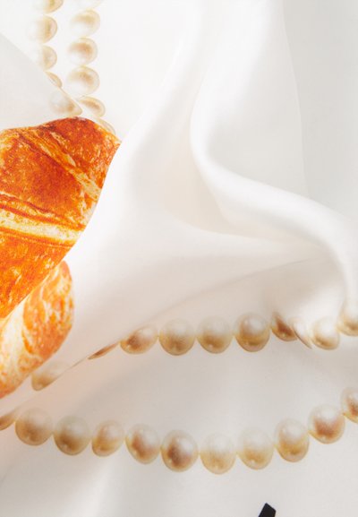 Zijde sjaal met een print van een croissant en parelachtige kralen op een witte achtergrond, met een zachte textuur en levendige kleuren.