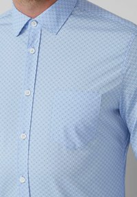 Hellblaues Button-up-Hemd mit einem kleinen Pünktchenmuster. Verfügt über eine Brusttasche und weiße Knöpfe, aus einem glatten Stoff gefertigt.