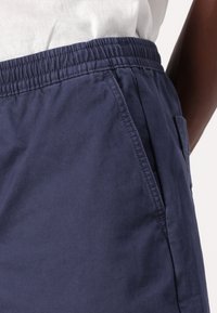 Mørkeblå shorts laget av bomullsstoff, med elastisk midje, sidelommer og en glatt tekstur. Ren, enkel design.