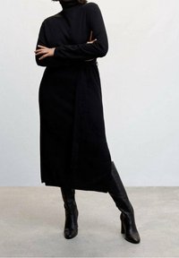 Robe noire à manches longues avec col montant et ceinture à la taille. Accompagnée de bottes noires montant jusqu'aux genoux. Texture lisse et design minimaliste.