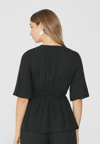 Schwarzes Peplum-Oberteil aus strukturiertem Stoff, mit kurzen Ärmeln und elastischem Bund. Mit rundem Halsausschnitt und dezenten vertikalen Streifen.