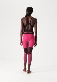 Black sports bra with cut-out back, paired with pink and maroon leggings featuring mesh panels and contrasting seams.