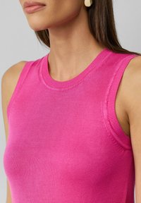 Dopasowany bezrękawnik w jaskrawym różu, wykonany z miękkiej dzianiny. Posiada okrągły dekolt oraz prążkowane wykończenia przy armiach i dekolcie.