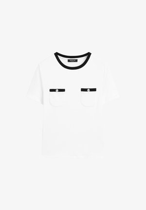 Weißes T-Shirt mit schwarzer runder Ausschnitt, zwei Brusttaschen mit schwarzem Besatz und silbernen Knöpfen. Kurze Ärmel, schlichtes Design.