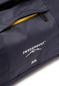 Laaverebeige kott, valmistatud vastupidavast kangast, millel on kollane lukktasku. Omab valget "SWEDEMOUNT" logo ja "30L" teksti. Kompaktne, ristkülikukujuline kuju.