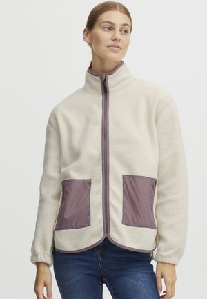 Fleece jacket in cream with purple accents. Features zip closure, high collar, and two front pockets with purple fabric. Soft texture.