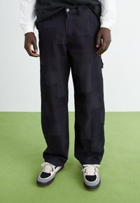 Navy cargo pants with a geometric pattern, made of cotton blend fabric. Features side pockets and a relaxed fit, paired with multicolored sneakers.