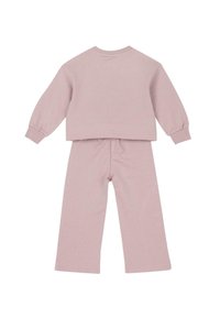 Světlý růžový bavlněný loungewear set obsahující top s dlouhým rukávem a kulatým výstřihem a široké kalhoty s elastickým pasem a žebrovanými manžetami a lemem.