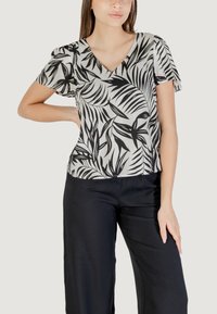 Blusa a maniche corte bianca e nera con scollo a V e motivo a foglie, abbinata a pantaloni neri larghi. Tessuto liscio e leggero.