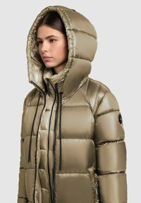 Geacă puffer în verde metalizat măsliniu cu un design căptușit, glugă ajustabilă, fermoar negru și șnururi de ajustare, având un logo pe mânecă.