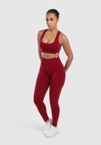 Červená sportovní podprsenka a legíny s vysokým pasem vyrobené z elastického materiálu. Outfit má bezešvý design a minimalistické logo na pásu.