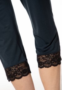 Schwarze Caprihosen mit Spitzenbesatz aus einem weichen, dunklen Stoff. Die Spitze hat einen gewellten Rand und ein filigranes Blumenmuster am Saum.