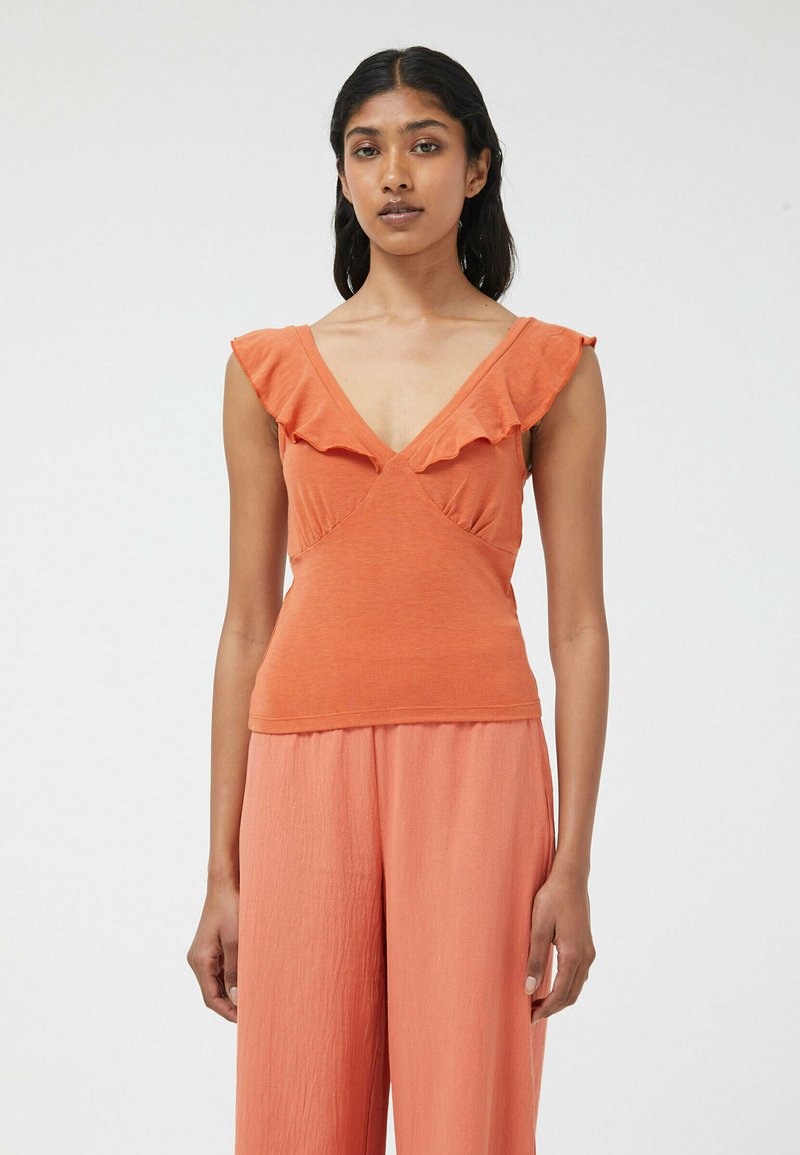 Top naranja sin mangas con bordes arrugados, diseño de escote en V, material de algodón suave, torso ajustado y textura lisa. Combinado con pantalones de melocotón sueltos.