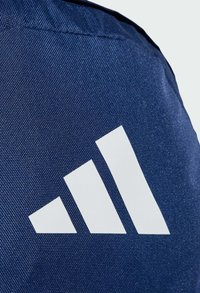 Tessuto blu scuro con una finitura testurizzata, caratterizzato da un grande logo bianco a tre strisce. Il design enfatizza linee pulite e un forte contrasto.