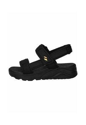 Sandalia negra de punta abierta con suela gruesa y correas ajustables sobre el pie y el talón, con un pequeño logo amarillo en la correa lateral.