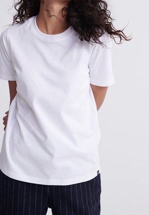 White cotton t-shirt with a round neckline, short sleeves, and a relaxed fit. Navy striped pants visible below. Simple design, no patterns.
