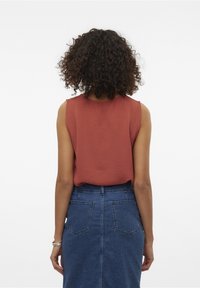 Haut sans manches couleur rouille avec tissu texturé, associé à une jupe en denim bleu taille haute avec deux poches à l'arrière.