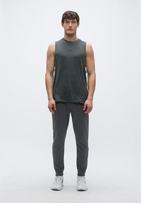 Tumši pelēks sporta topiņš bez piedurknēm ar apaļu izgriezumu, savienots ar pieguļošām pelēkām sporta biksēm. Valkāts ar baltām sporta kurpēm. Vienkāršs dizains, minimāla zīmola redzamība.