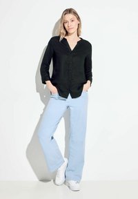 Camicia in lino nera con scollo a V e chiusura con bottoni, abbinata a pantaloni dalla gamba larga di un blu chiaro e sneaker bianche. Outfit casual con tasche.