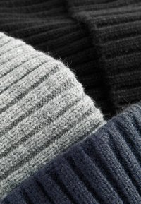 Trys megztos beanies pilkos, juodos ir tamsiai mėlynos spalvos, su tekstūriniais raukiniais, pagamintos iš minkštos, vilnai panašios medžiagos.
