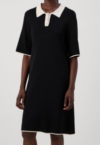 Abito nero con collo a camicia, maniche corte e rifiniture beige. Presenta una chiusura a bottoni al collo e una vestibilità comoda.