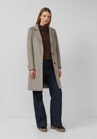 Grauer Wollmantel mit maßgeschneidertem Design, einreihiger Vorderseite und Revers mit Kerbe. Kombiniert mit dunkelblauen Jeans mit weitem Bein und schwarzen Plateau-Stiefeln.