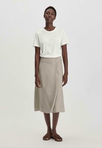 T-shirt blanc à manches courtes en coton, associé à une jupe enveloppante en lin beige clair arrivant au genou. Des sandales complètent la tenue.