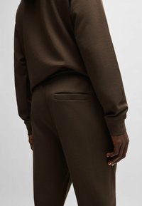 Bruine sweatshirt en bijpassende broek gemaakt van zacht, gestructureerd materiaal. De broek heeft een enkele achterzak met een afgeronde rand.