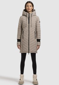 Abrigo acolchado beige con acolchado en forma de chevron, cremallera frontal y capucha ajustable. Los puños negros y los bolsillos laterales completan el diseño.