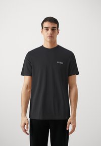 Fekete pamut póló kerek nyakú, rövid ujjú, bal mellen kis fehér "GUESS" logóval nyomtatva.