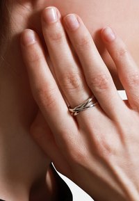 Anello d'argento con bande intrecciate poggia su una mano. Texture liscia, finitura lucida e design semplice sono caratteristiche principali. Unghie naturali visibili.