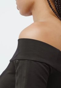 Mustapaita ilman olkasaumoja, jossa on sileä kangas, istuva muotoilu ja hieman rento kaula-aukko, joka korostaa hienoa kiiltoa ja räätälöityä istuvuutta.