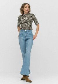 Top i leopardmønster med korte ærmer, parret med høj-waist, lyseblå, flagrende jeans og brune ankelstøvler. Ensfarvet hvid baggrund.