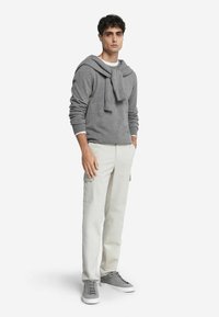 Szary sweter z detalem w postaci szalika noszony na białej koszulce, w połączeniu z beżowymi spodniami cargo i szarymi trampkami. Prosty i swobodny design.