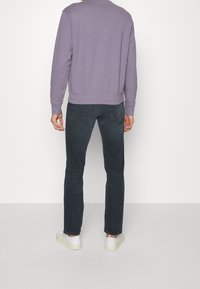 Felpa viola, in misto cotone, collo giro, polsini a coste, abbinata a jeans di denim grigio scuro e sneakers bianche. Design semplice, aspetto casual.