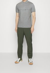 Polo gris avec le logo "HACKETT", pantalon vert et baskets blanches avec des accents verts et des semelles en caoutchouc marron. Design simple et ajusté.