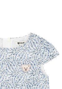Robe blanche avec motif floral bleu, textile doux, manches courtes bouffantes et appliqué d'ours brodé à l'avant. Étiquette Steiff visible.